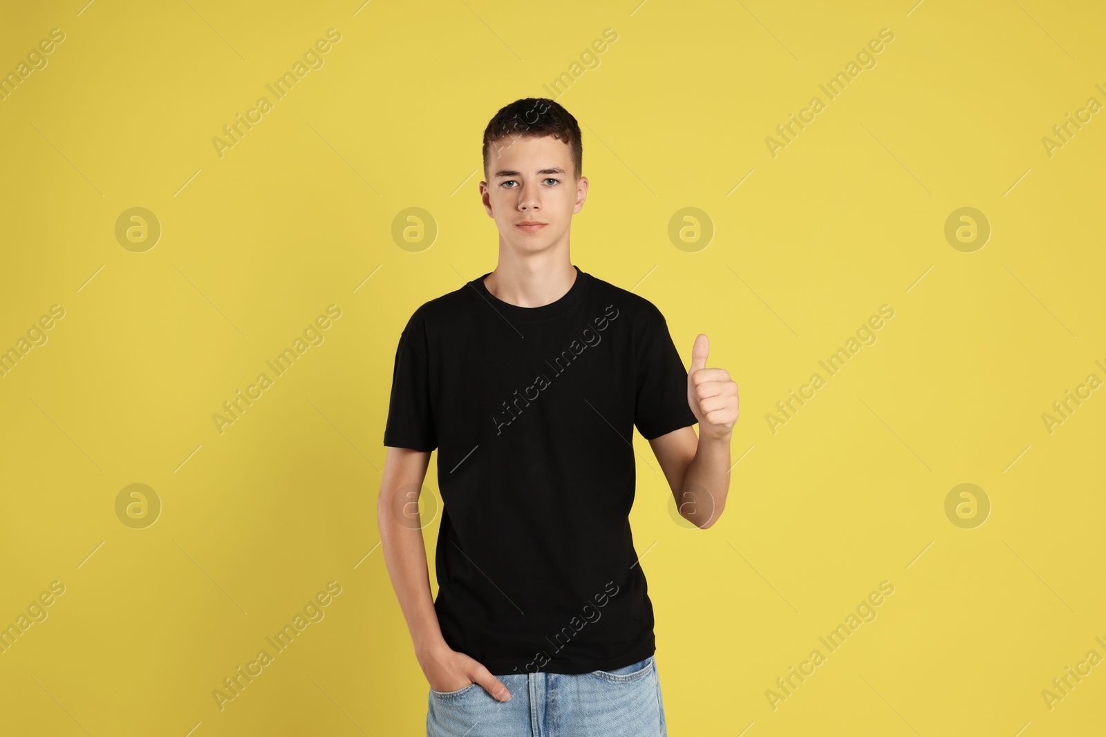 Photo of Teenage boy wearing black t-shirt and showing thumbs up on yellow background