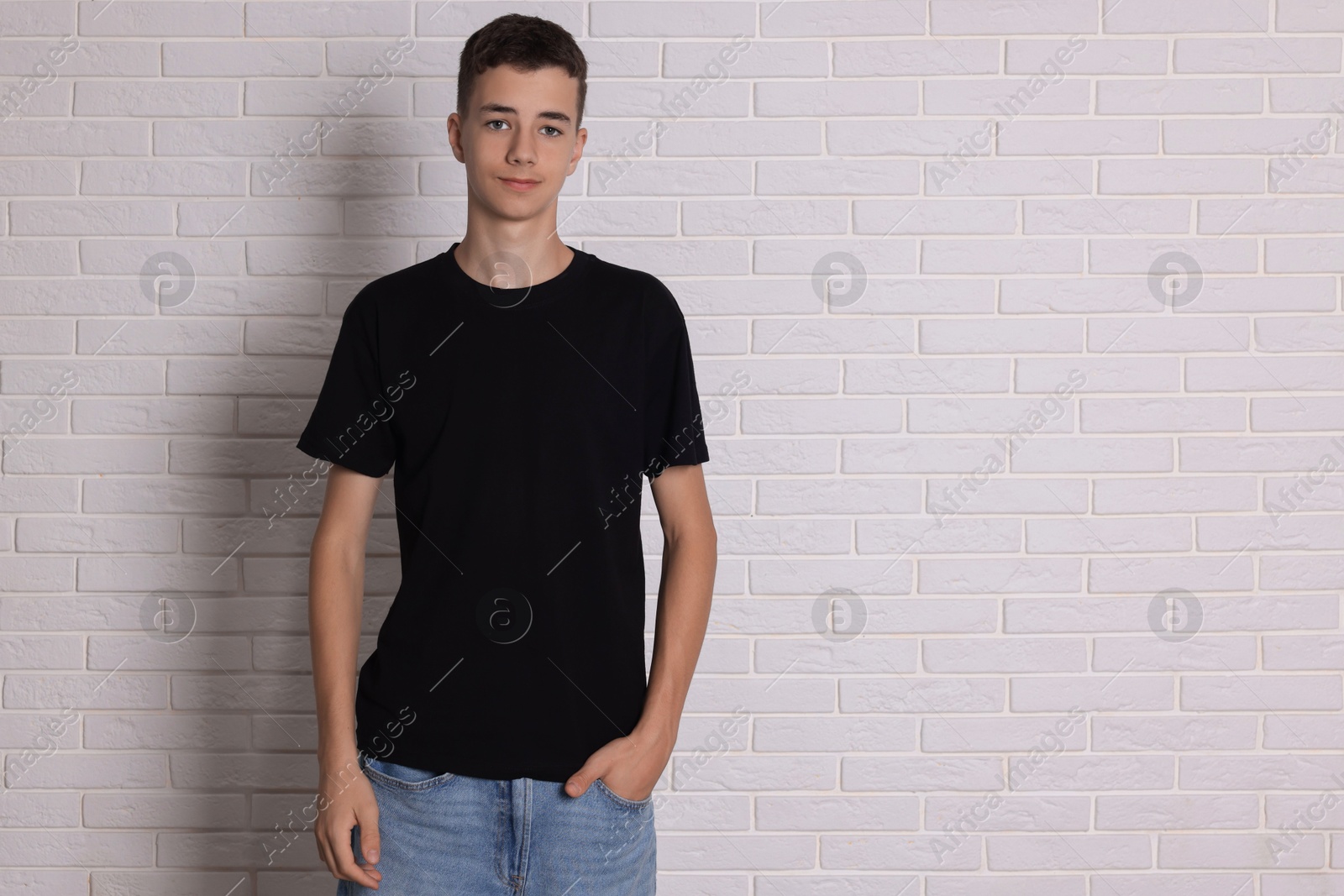 Photo of Teenage boy wearing black t-shirt near white brick wall, space for text