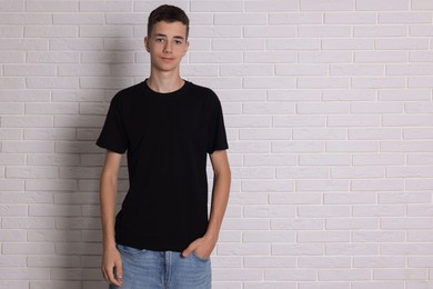 Photo of Teenage boy wearing black t-shirt near white brick wall, space for text