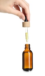 Photo of Woman dripping tincture from pipette into bottle on white background, closeup