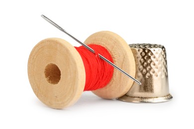 Photo of Thimble and needle with red sewing thread isolated on white, closeup