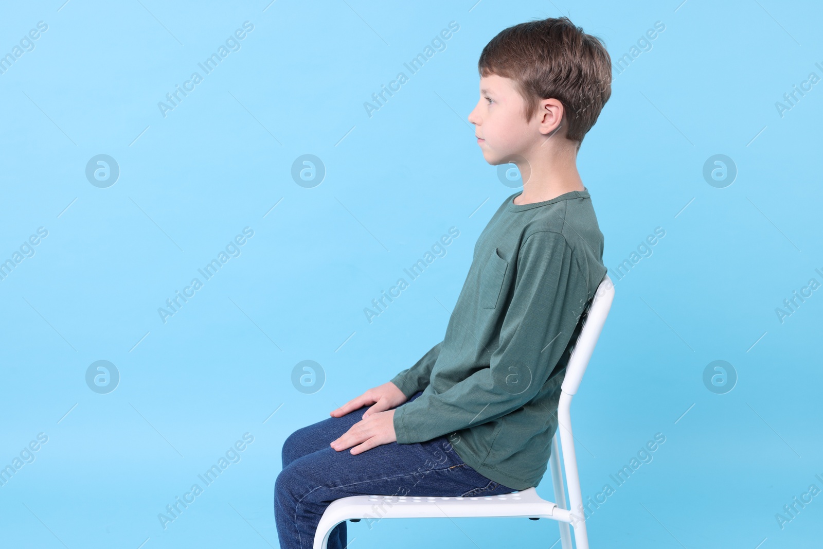 Photo of Boy with correct posture sitting on chair against light blue background