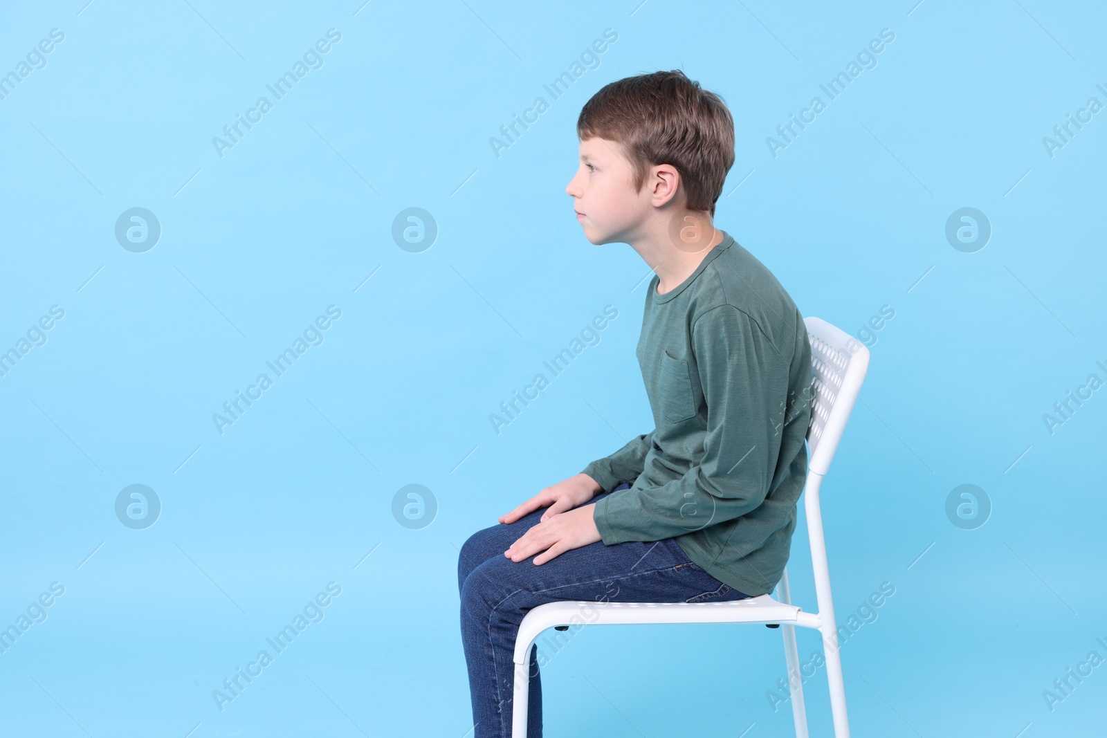 Photo of Boy with incorrect posture sitting on chair against light blue background