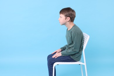 Boy with incorrect posture sitting on chair against light blue background