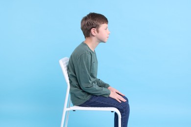 Photo of Boy with incorrect posture sitting on chair against light blue background