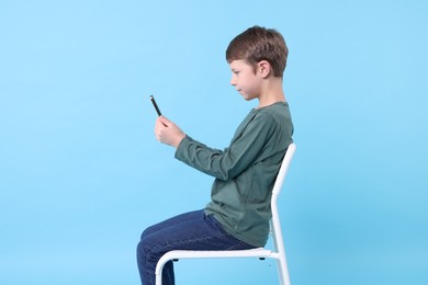 Photo of Boy with correct posture and phone sitting on chair against light blue background