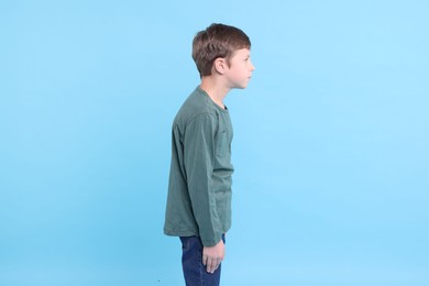 Boy with incorrect posture on light blue background