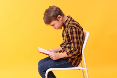 Boy with incorrect posture reading book on chair against yellow background