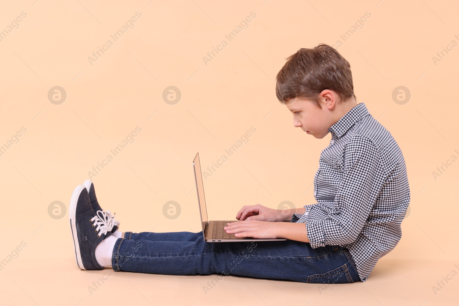 Photo of Boy with incorrect posture and laptop sitting on beige background