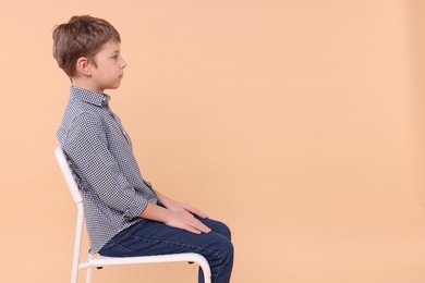 Boy with correct posture sitting on chair against beige background