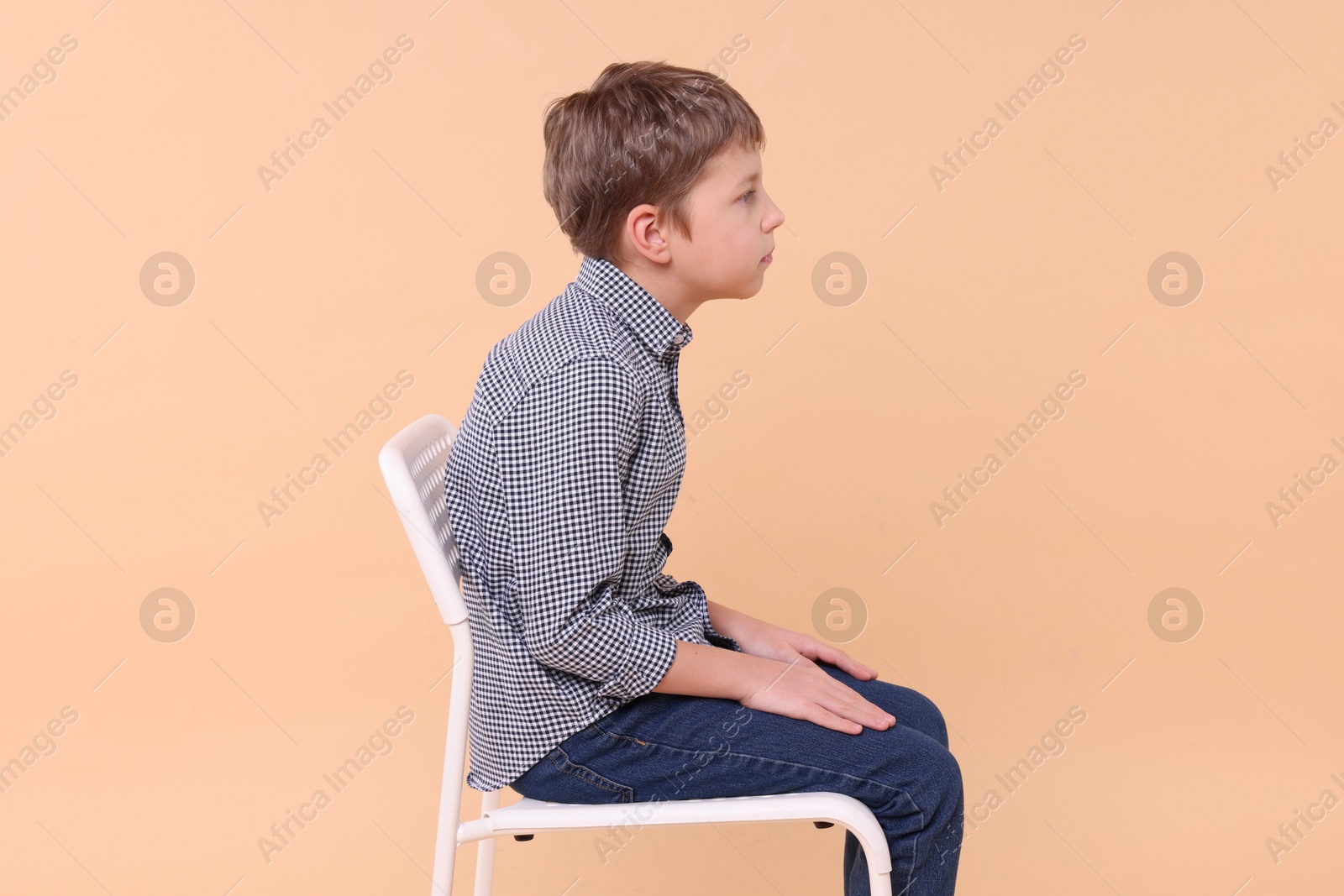 Photo of Boy with incorrect posture sitting on chair against beige background