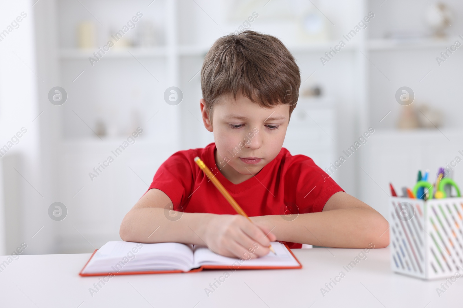 Photo of Boy with correct posture doing homework at white desk indoors