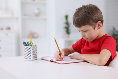 Boy with correct posture doing homework at white desk indoors