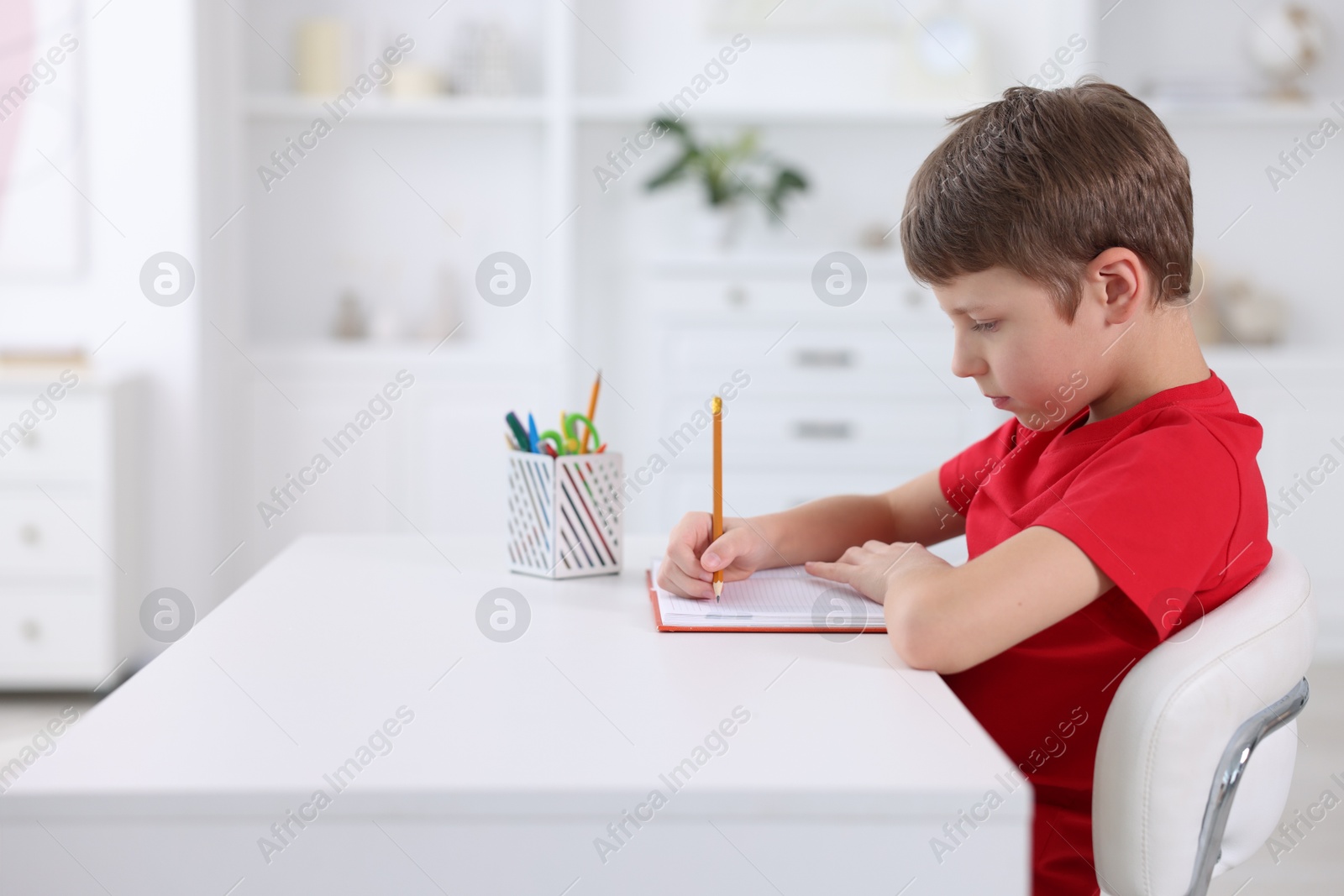 Photo of Boy with correct posture doing homework at white desk indoors