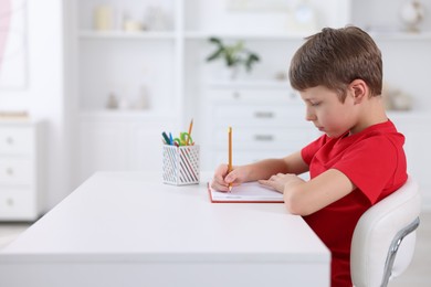 Boy with correct posture doing homework at white desk indoors