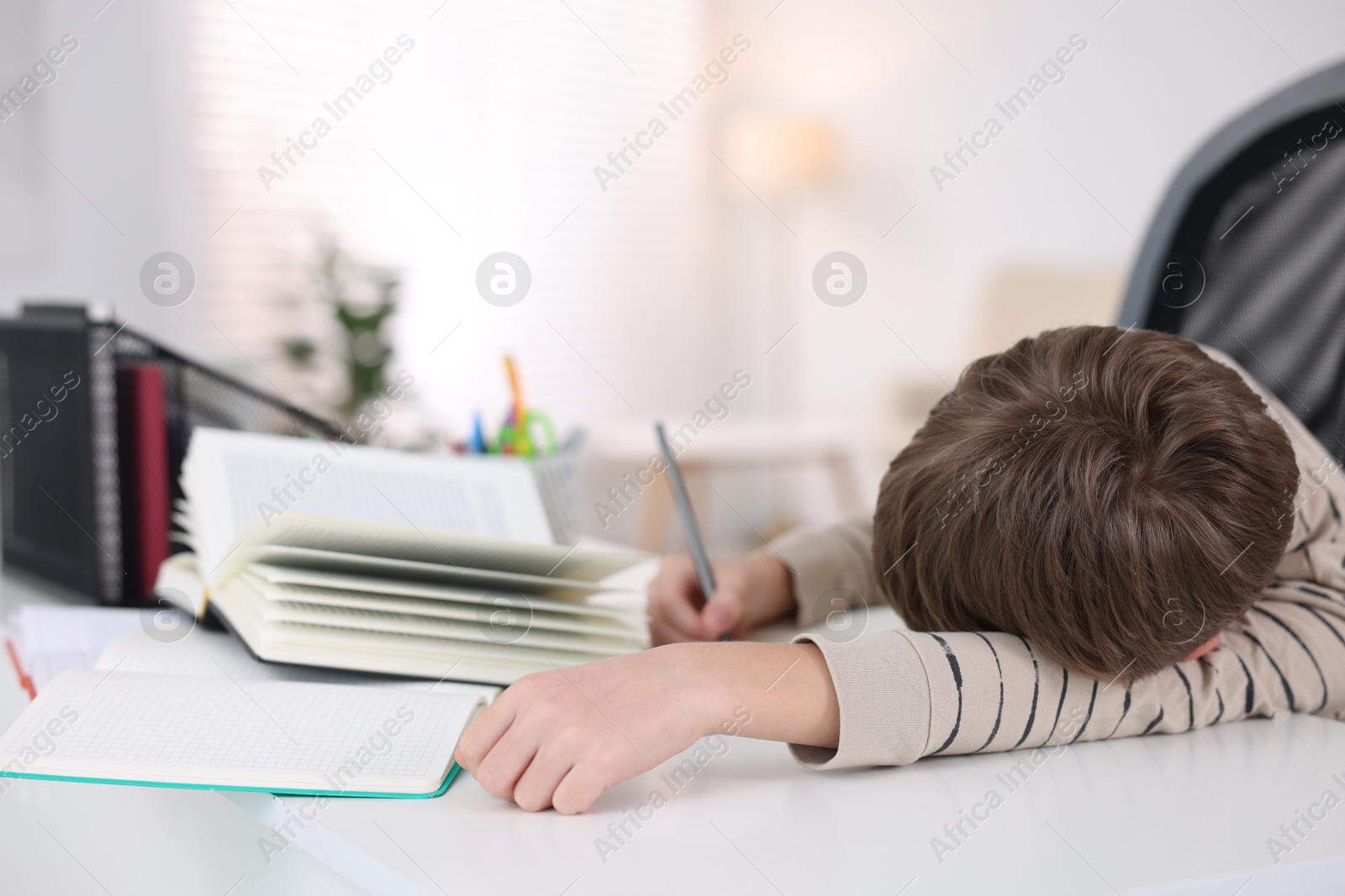 Photo of Boy with incorrect posture doing homework at white desk indoors