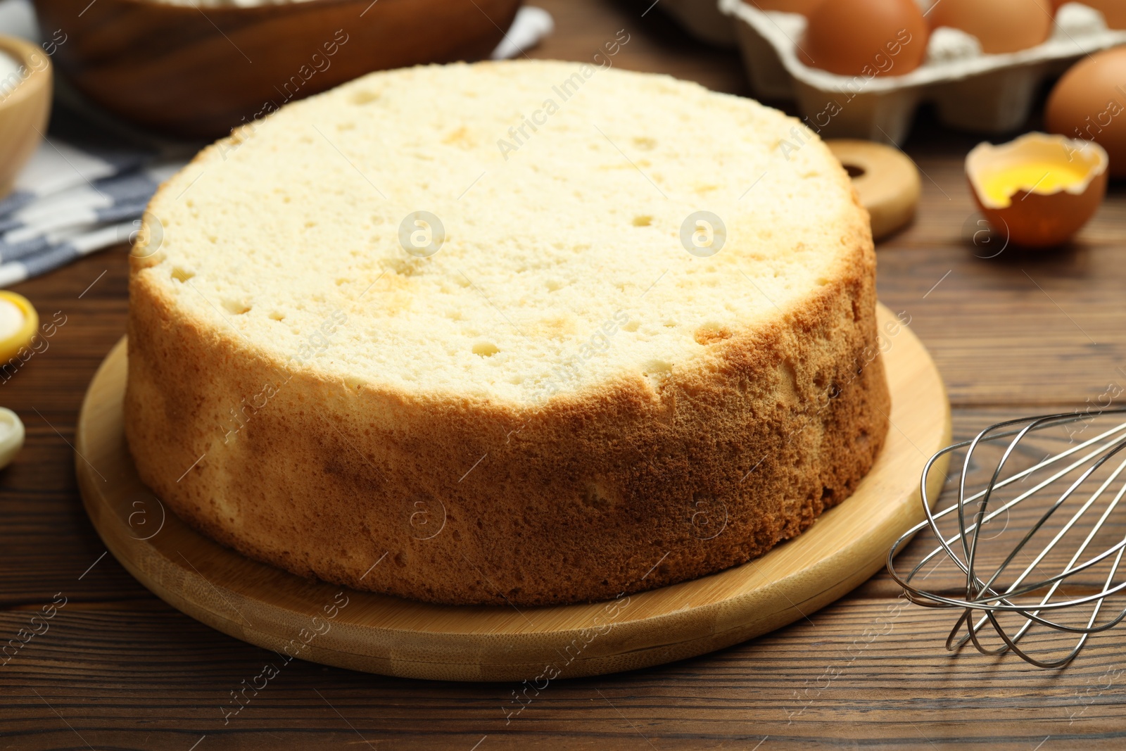 Photo of Tasty cut sponge cake, whisk and ingredients on wooden table