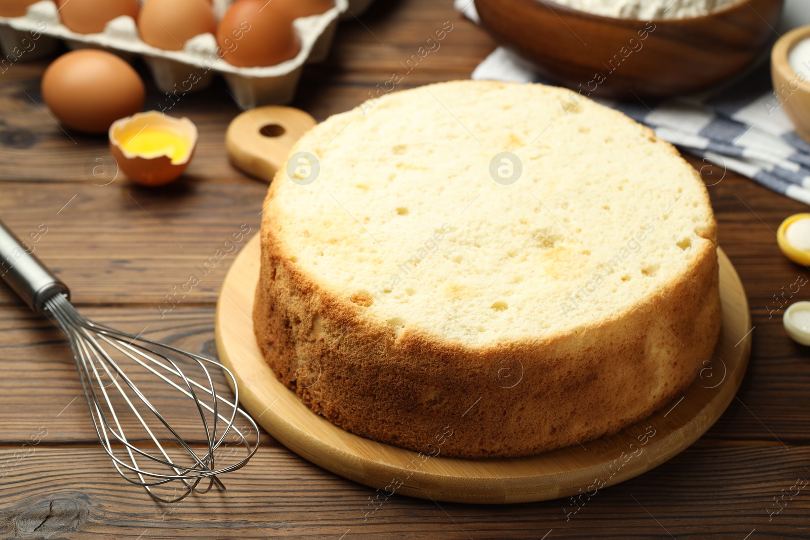 Photo of Tasty cut sponge cake, whisk and ingredients on wooden table