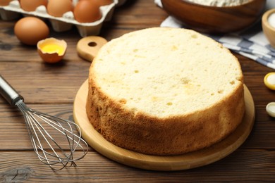 Photo of Tasty cut sponge cake, whisk and ingredients on wooden table