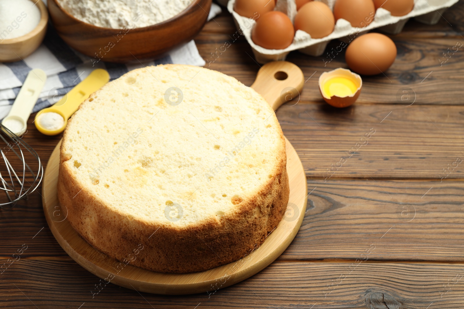 Photo of Tasty cut sponge cake and ingredients on wooden table