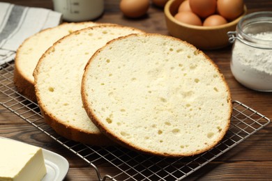 Photo of Tasty cut sponge cake and ingredients on wooden table, closeup