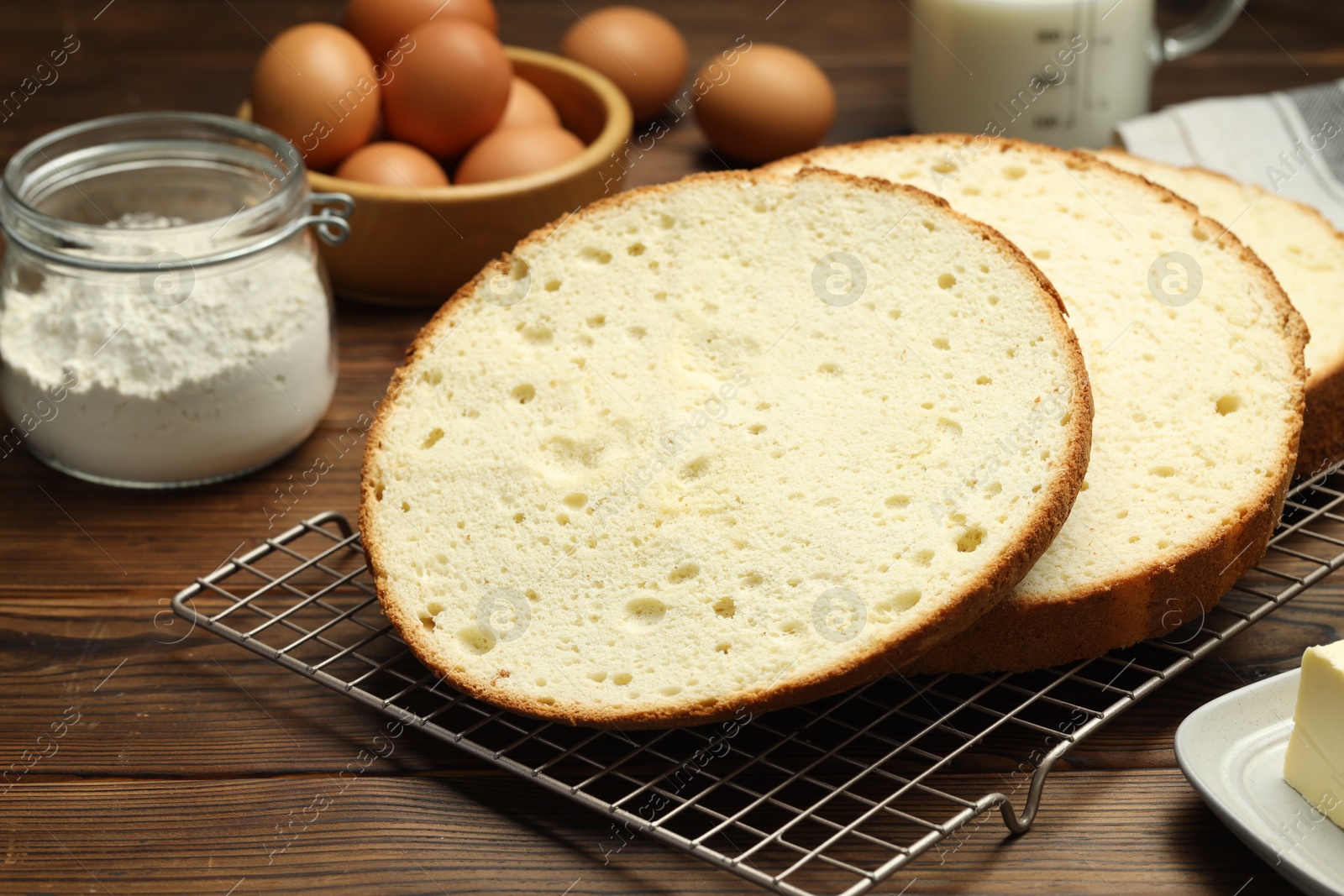 Photo of Tasty cut sponge cake and ingredients on wooden table, closeup