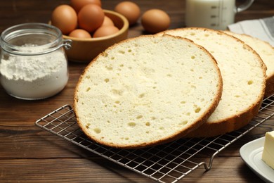 Photo of Tasty cut sponge cake and ingredients on wooden table, closeup