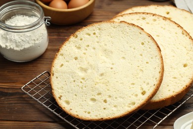 Photo of Tasty cut sponge cake and ingredients on wooden table, closeup