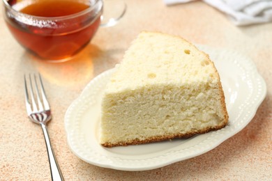 Photo of Piece of delicious sponge cake served on beige textured table, closeup