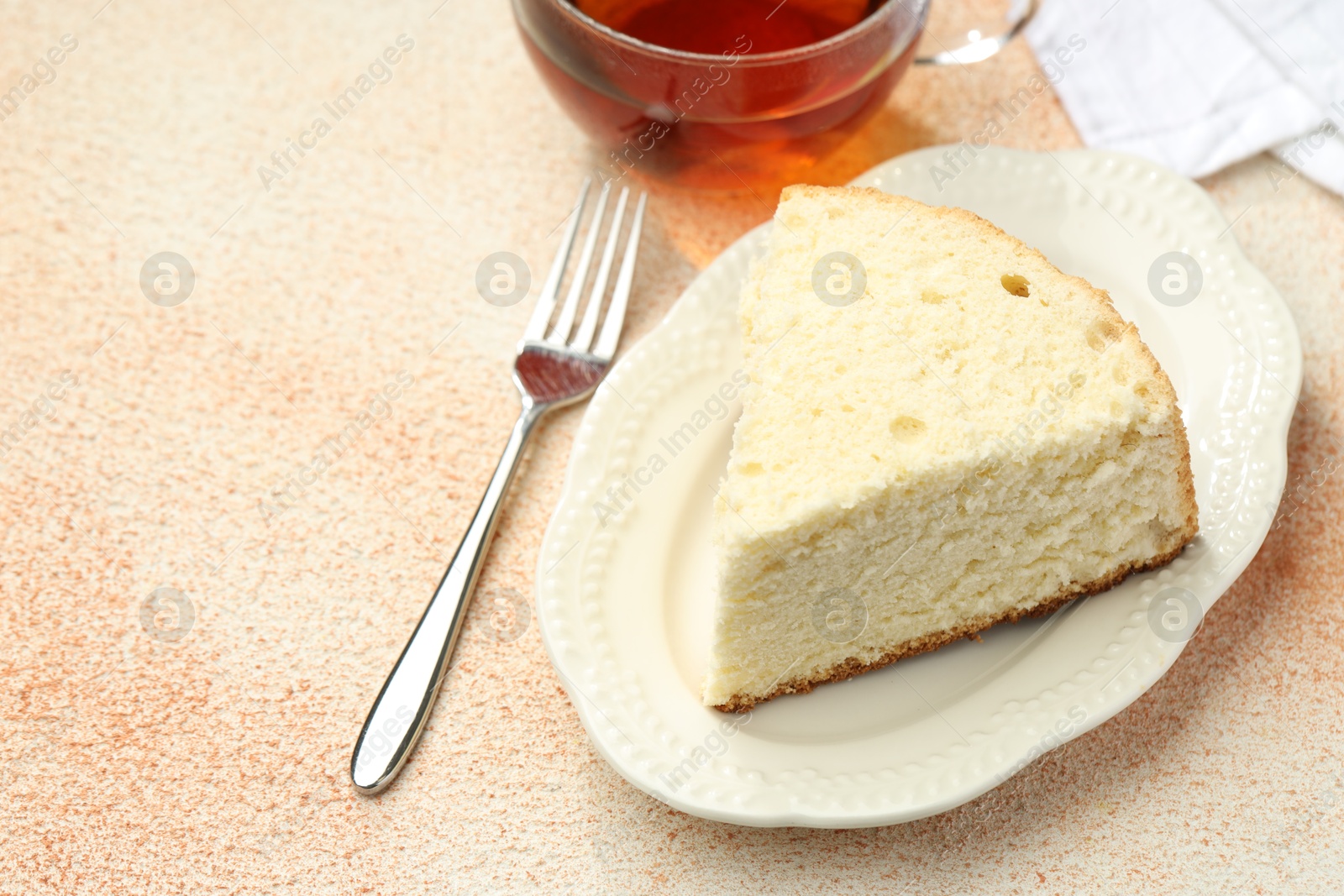 Photo of Piece of delicious sponge cake served on beige textured table, closeup