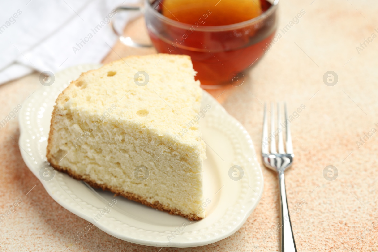 Photo of Piece of delicious sponge cake served on beige textured table, closeup