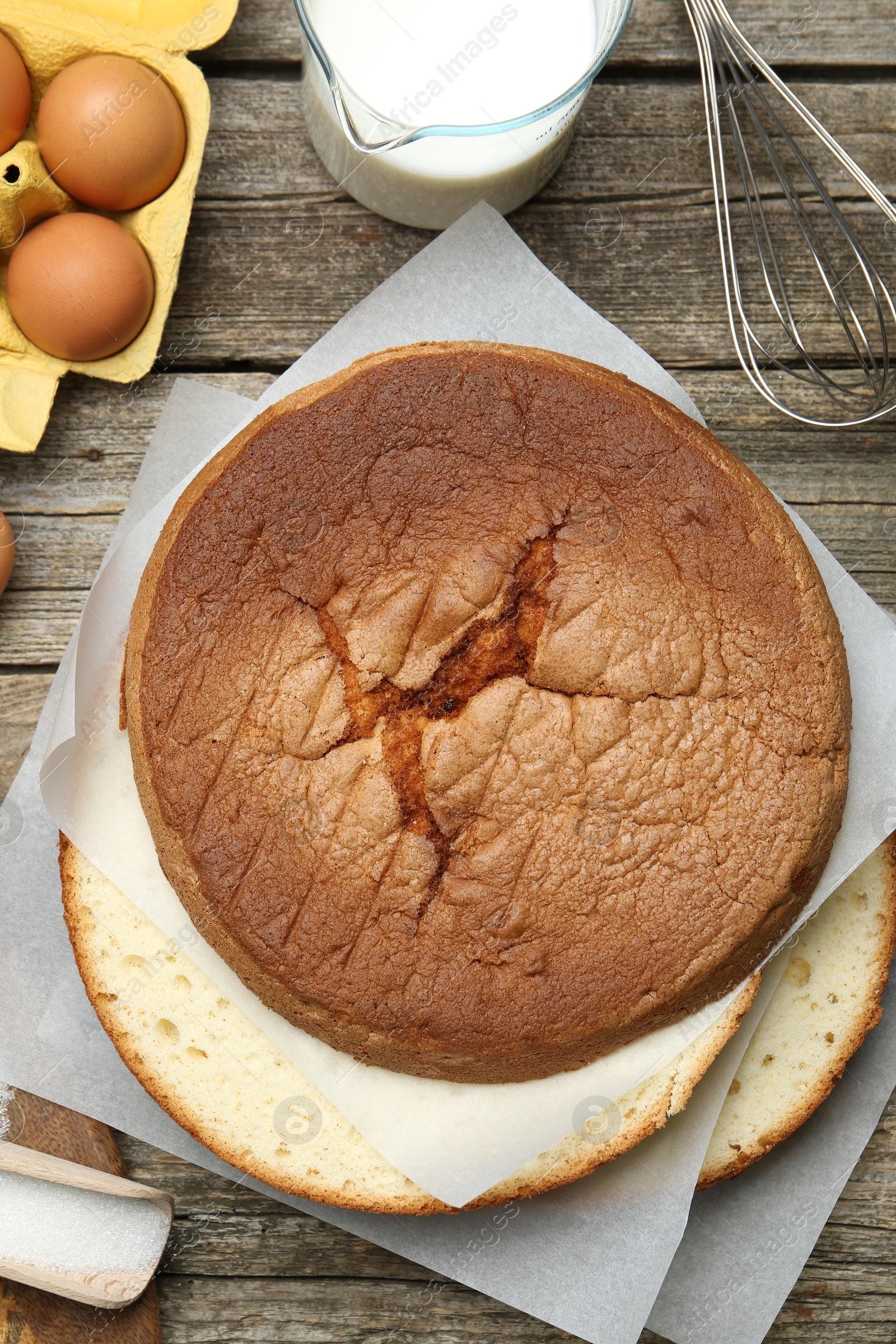 Photo of Delicious cut sponge cake, whisk and ingredients on wooden table, flat lay