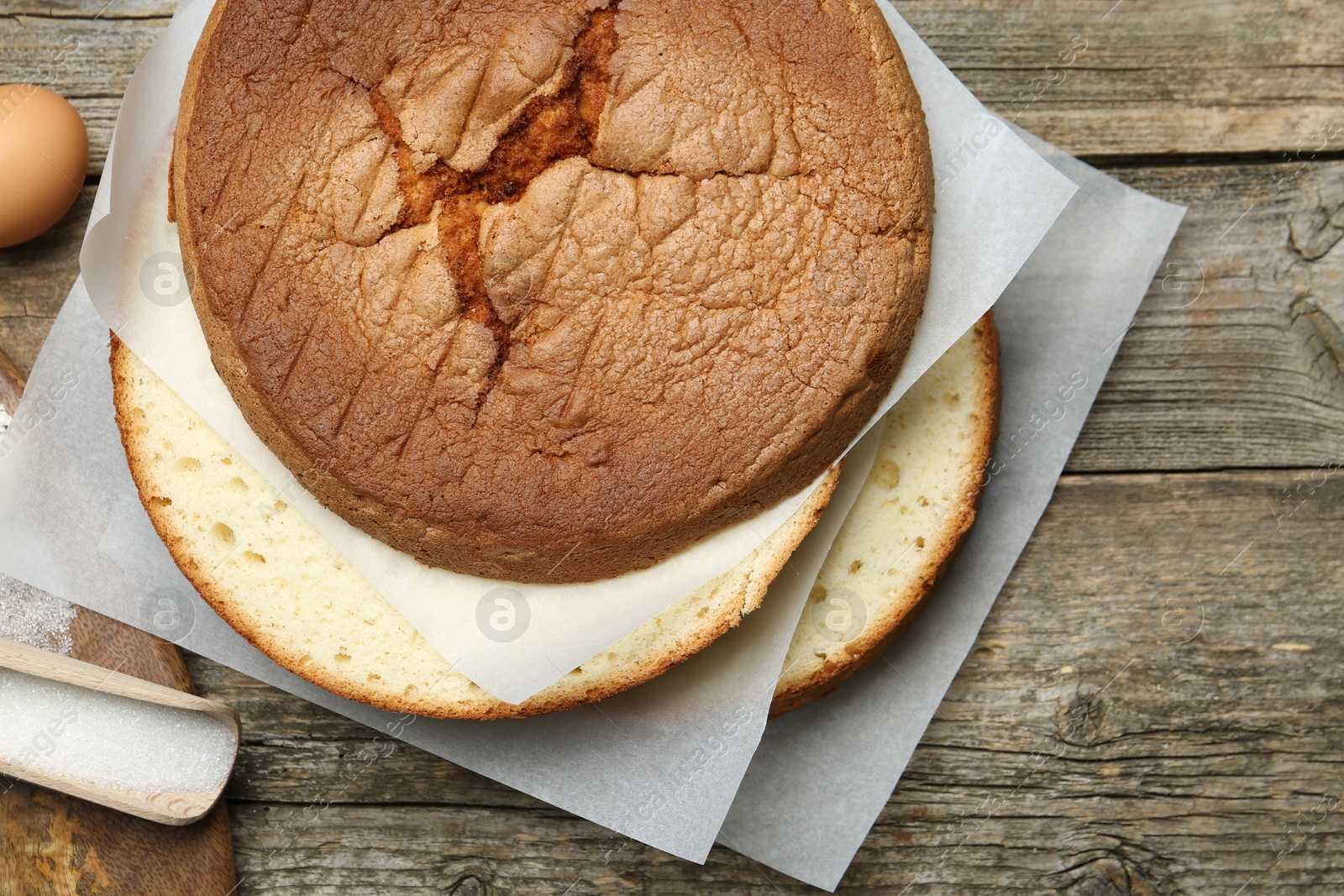 Photo of Delicious cut sponge cake and ingredients on wooden table, flat lay