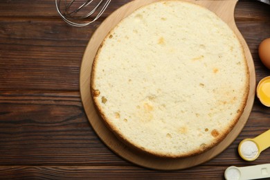 Photo of Delicious cut sponge cake and ingredients on wooden table, flat lay