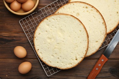 Photo of Delicious cut sponge cake, knife and ingredients on wooden table, flat lay