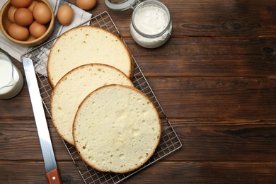 Photo of Delicious cut sponge cake, knife and ingredients on wooden table, flat lay. Space for text