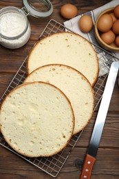 Photo of Delicious cut sponge cake, knife and ingredients on wooden table, flat lay