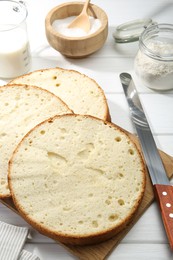 Photo of Delicious cut sponge cake and knife on white wooden table