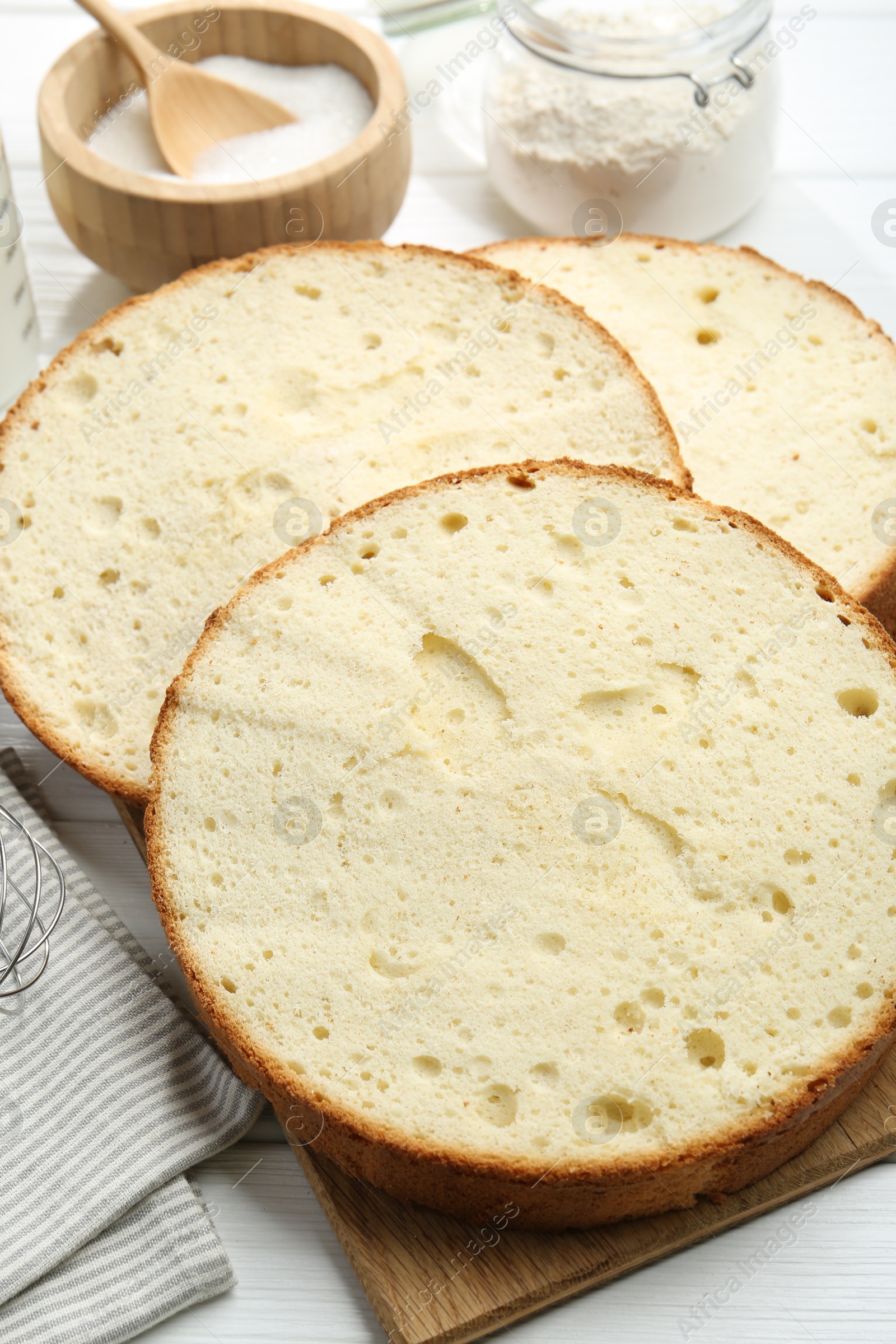 Photo of Delicious cut sponge cake and ingredients on white wooden table