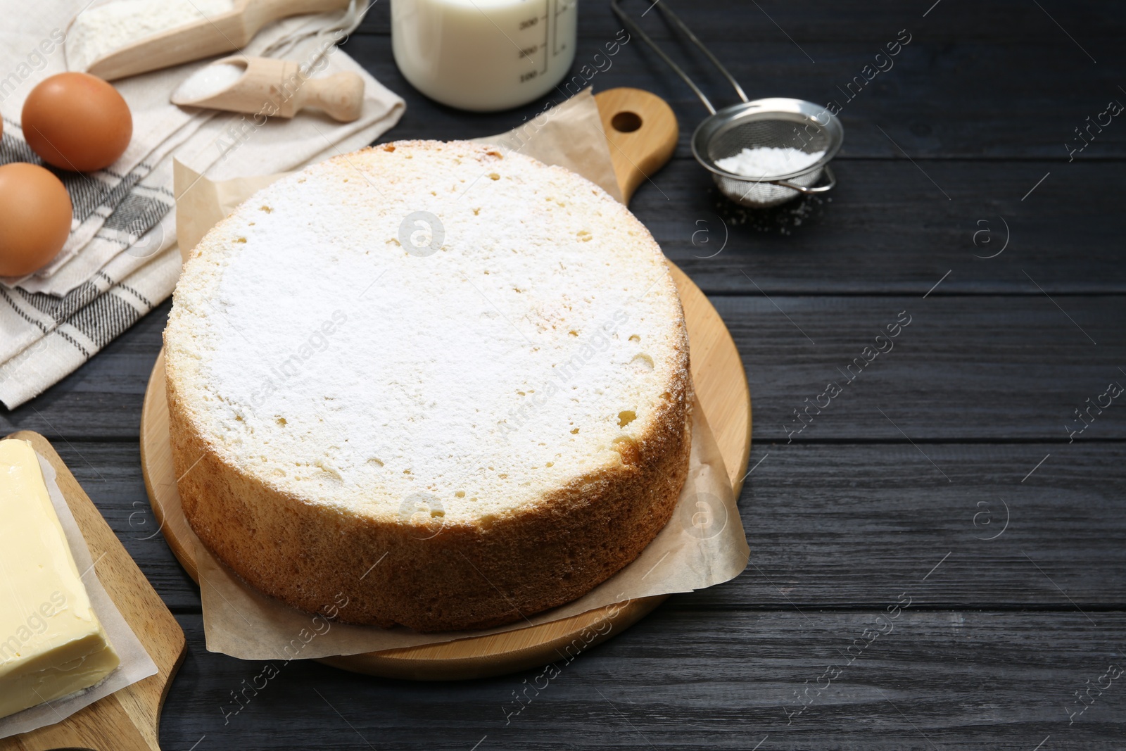 Photo of Delicious sponge cake and ingredients on black wooden table