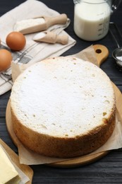 Photo of Delicious sponge cake and ingredients on black wooden table