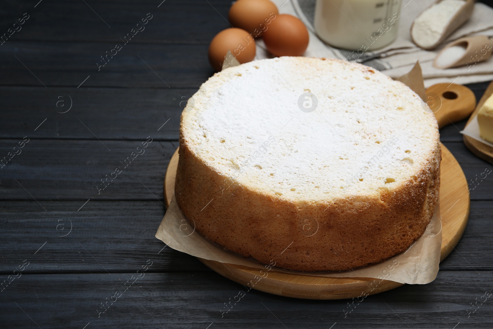 Photo of Delicious sponge cake and ingredients on black wooden table