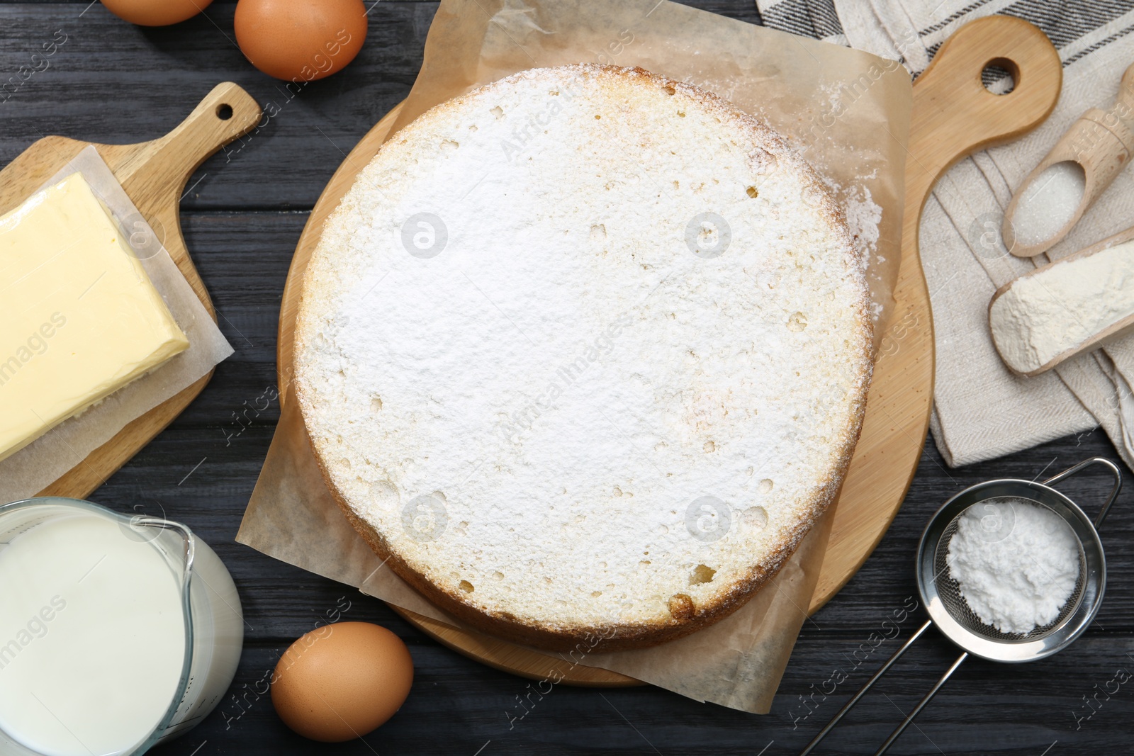 Photo of Delicious sponge cake and ingredients on black wooden table, flat lay