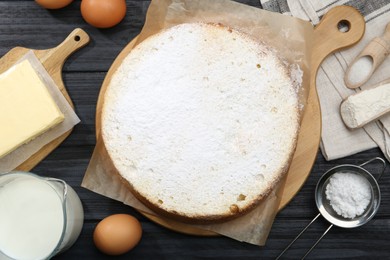 Photo of Delicious sponge cake and ingredients on black wooden table, flat lay