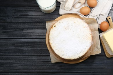 Delicious sponge cake with powdered sugar and ingredients on black wooden table, flat lay. Space for text