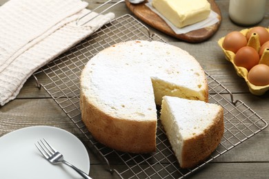 Delicious cut sponge cake, fork and ingredients on wooden table