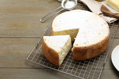 Photo of Delicious cut sponge cake with powdered sugar on wooden table