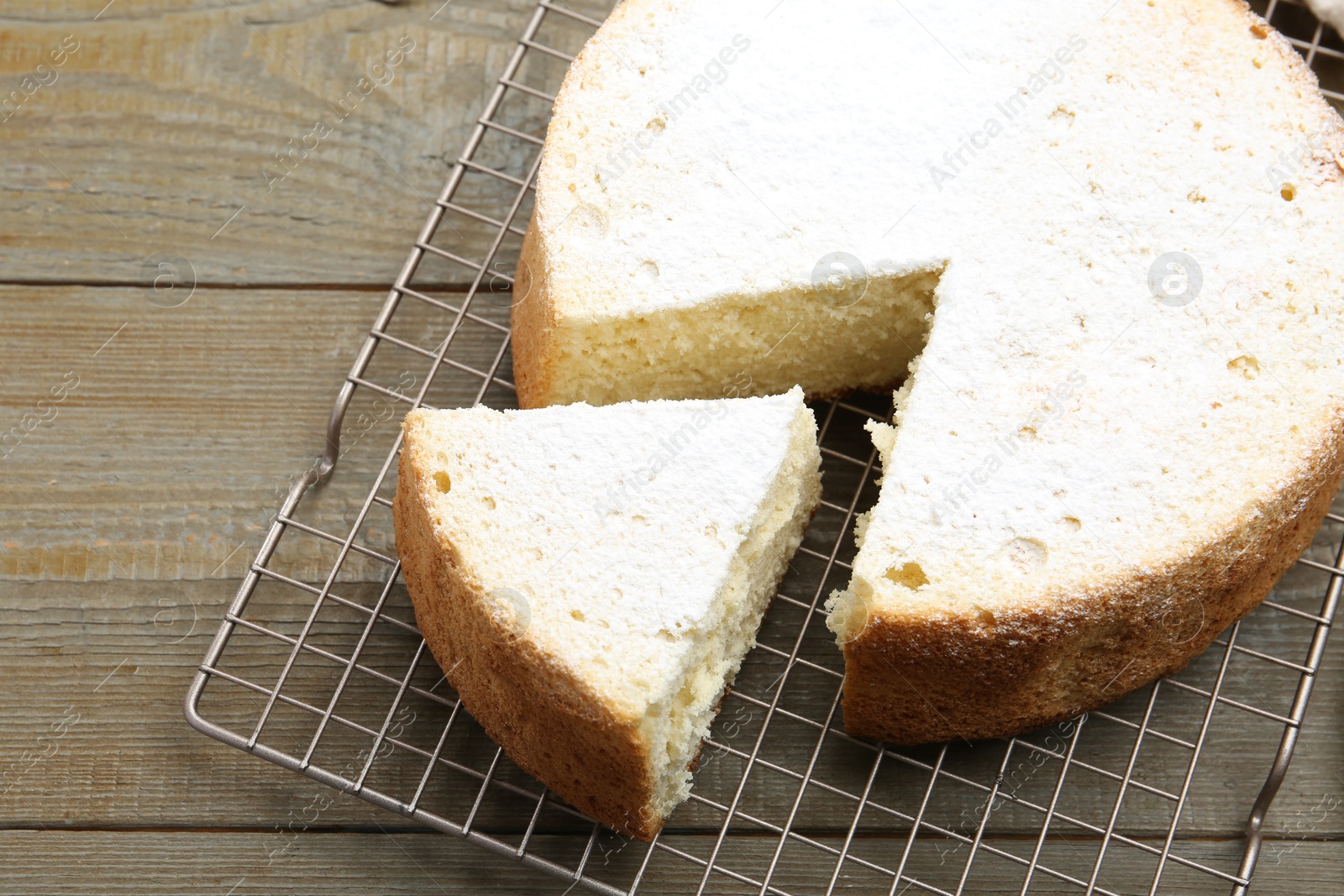 Photo of Delicious cut sponge cake with powdered sugar on wooden table