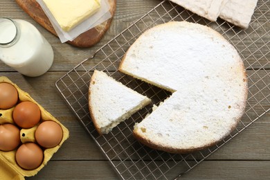 Photo of Delicious cut sponge cake and ingredients on wooden table, flat lay