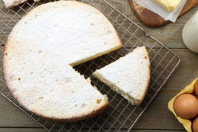 Delicious cut sponge cake and ingredients on wooden table, flat lay